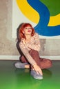 Young redhead Caucasian woman in retro style of 70s sitting at wall vertical looking into camera head up Royalty Free Stock Photo