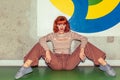 Young redhead Caucasian woman in retro style of 70s sitting at walll horizontal hands down and looking into camera Royalty Free Stock Photo
