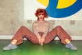 Young redhead Caucasian woman in retro style of 70s sitting at walll horizontal looking into camera Royalty Free Stock Photo