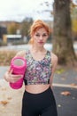 Young redhead confident sportswoman holding a foam roller in the park at autumn