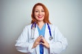 Young redhead doctor woman using stethoscope over white isolated background Hands together and fingers crossed smiling relaxed and Royalty Free Stock Photo