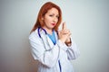 Young redhead doctor woman using stethoscope over white isolated background Holding symbolic gun with hand gesture, playing Royalty Free Stock Photo