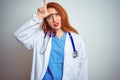 Young redhead doctor woman using stethoscope over white isolated background making fun of people with fingers on forehead doing Royalty Free Stock Photo