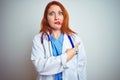 Young redhead doctor woman using stethoscope over white isolated background Pointing aside worried and nervous with forefinger,