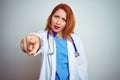 Young redhead doctor woman using stethoscope over white isolated background pointing displeased and frustrated to the camera,
