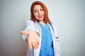 Young redhead doctor woman using stethoscope over white isolated background smiling cheerful offering palm hand giving assistance Royalty Free Stock Photo