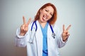 Young redhead doctor woman using stethoscope over white isolated background smiling with tongue out showing fingers of both hands Royalty Free Stock Photo