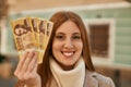 Young redhead girl smiling happy holding hungarian forint banknotes at the city