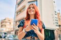 Young redhead girl smiling happy using smartphone at the city