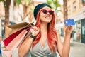 Young redhead girl wearing french style holding shopping bags  and showing credit card at the city Royalty Free Stock Photo