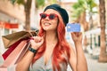 Young redhead girl wearing french style holding shopping bags  and showing credit card at the city Royalty Free Stock Photo