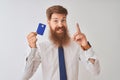 Young redhead irish businessman holding credit card standing over isolated white background surprised with an idea or question Royalty Free Stock Photo