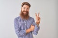 Young redhead irish man wearing casual shirt standing over isolated white background smiling with happy face winking at the camera Royalty Free Stock Photo