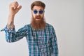 Young redhead irish man wearing casual shirt and sunglasses over isolated white background angry and mad raising fist frustrated Royalty Free Stock Photo