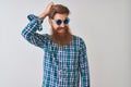 Young redhead irish man wearing casual shirt and sunglasses over isolated white background confuse and wonder about question