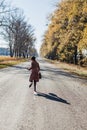 Young redhead lady woman in pink vintage coat and hat with suitcase in retro style running away along a park road with golden