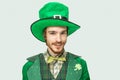 Young redhead man in green saint Patrick`s costume and hat look straight on camera. on white background.