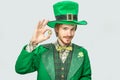 Young redhead man hold golden 100 coin and look on camera. He quite happy. Guy wear green saint Patrick`s suit.