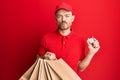 Young redhead man holding delivery bags and countdown clock looking at the camera blowing a kiss being lovely and sexy