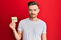 Young redhead man holding sticker with vegan word thinking attitude and sober expression looking self confident