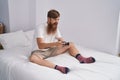 Young redhead man playing video game sitting on bed at bedroom Royalty Free Stock Photo