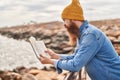 Young redhead man reading book with serious expression at seaside Royalty Free Stock Photo