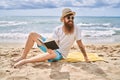 Young redhead man reading book sitting on the towel at the beach Royalty Free Stock Photo