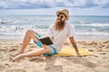 Young redhead man reading book sitting on the towel at the beach Royalty Free Stock Photo