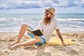 Young redhead man reading book sitting on the towel at the beach Royalty Free Stock Photo