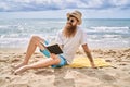 Young redhead man reading book sitting on the towel at the beach Royalty Free Stock Photo