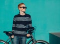 Young redhead man standing next to a vintage bicycle in suglasses near turquoise wall warm summer sunny day Royalty Free Stock Photo