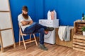 Young redhead man tired waiting for washing machine at laundry room