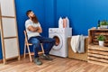 Young redhead man tired waiting for washing machine at laundry room