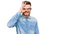 Young redhead man wearing casual denim shirt doing ok gesture with hand smiling, eye looking through fingers with happy face Royalty Free Stock Photo