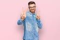 Young redhead man wearing casual denim shirt smiling looking to the camera showing fingers doing victory sign Royalty Free Stock Photo