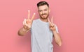 Young redhead man wearing casual grey t shirt smiling looking to the camera showing fingers doing victory sign Royalty Free Stock Photo