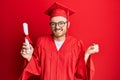 Young redhead man wearing graduation cap and ceremony robe holding degree screaming proud, celebrating victory and success very Royalty Free Stock Photo