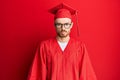 Young redhead man wearing red graduation cap and ceremony robe depressed and worry for distress, crying angry and afraid Royalty Free Stock Photo