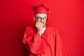 Young redhead man wearing red graduation cap and ceremony robe looking stressed and nervous with hands on mouth biting nails Royalty Free Stock Photo