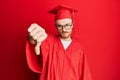 Young redhead man wearing red graduation cap and ceremony robe looking unhappy and angry showing rejection and negative with Royalty Free Stock Photo