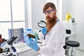 Young redhead man wearing scientist uniform holding marihuana weed with loupe at laboratory