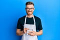 Young redhead man wearing waiter apron taking order smiling with a happy and cool smile on face