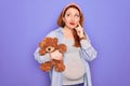 Young redhead pregnant woman expecting baby holding teddy bear over purple background serious face thinking about question, very Royalty Free Stock Photo