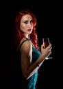 Young redhead woman in blue elegant dress holding wineglass with champagne and poses in a dark. Royalty Free Stock Photo