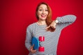 Young redhead student woman holding skate over red isolated background with surprise face pointing finger to himself Royalty Free Stock Photo