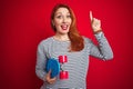 Young redhead student woman holding skate over red isolated background surprised with an idea or question pointing finger with Royalty Free Stock Photo