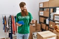 Young redhead volunteer man using touchpad holding canned food at charity center Royalty Free Stock Photo