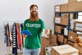 Young redhead volunteer man using touchpad holding canned food at charity center Royalty Free Stock Photo