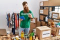Young redhead volunteer man using touchpad holding canned food at charity center Royalty Free Stock Photo