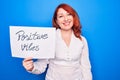 Young redhead woman asking for optimist attitude holding paper with positive vibes message looking positive and happy standing and